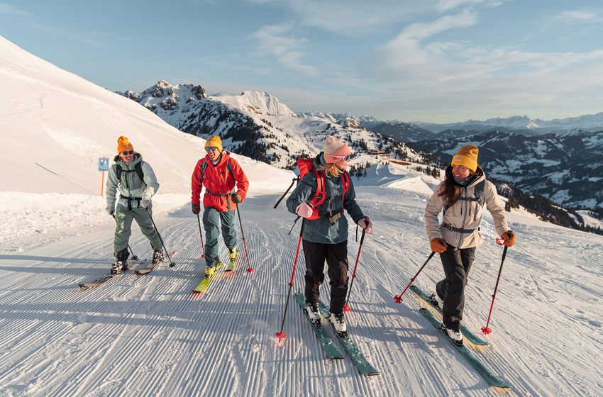 Vier Skitourengeher steigen bei Sonne eine präparierte Piste hinauf, umgeben von verschneiten Alpen | © Dorfgasteiner Bergbahnen AG