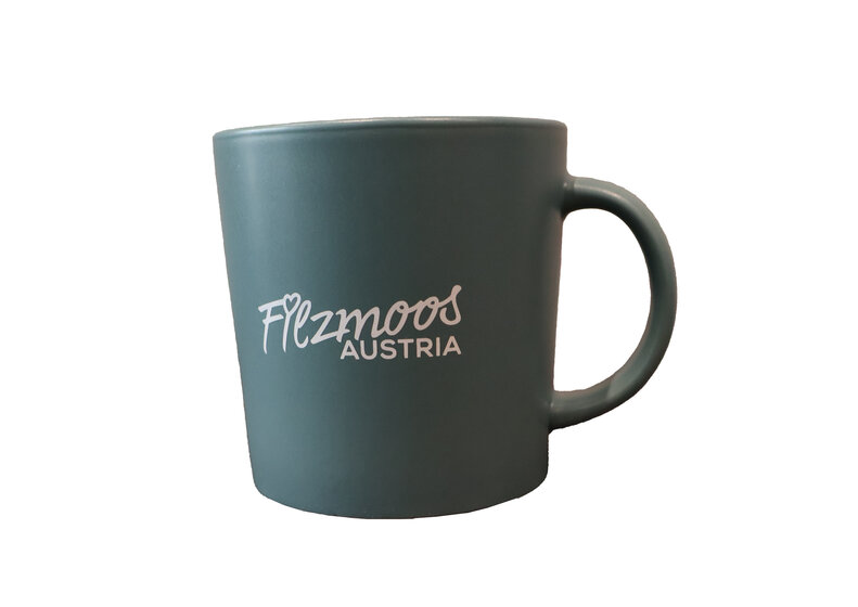 Dunkelgrüne Keramiktasse mit Filzmoos Austria Logo und Henkel, freigestellt vor hellem Hintergrund. | © Bergbahnen Filzmoos GmbH