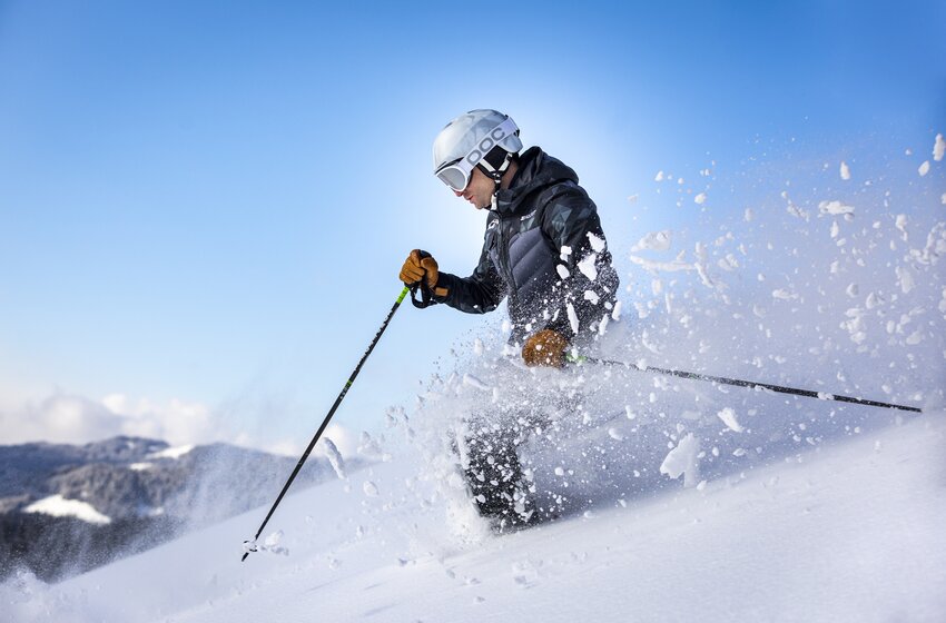Skifahrer mit weißem Helm pflügt bei Sonne durch frischen Pulverschnee, Schnee spritzt seitlich hoch. | © Bergbahnen Filzmoos GmbH