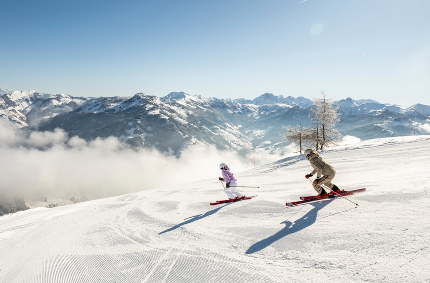 Zwei Skifahrerinnen fahren nebeneinander auf sonniger Piste mit Alpenblick | © Großarler Bergbahnen GmbH & Co KG