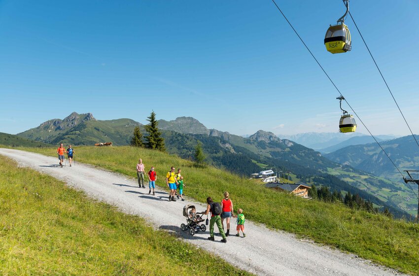 Wanderer mit Kindern und Kinderwagen auf Almweg in Großarl, gelbe Gondeln der Panoramabahn im Hintergrund | © Grossarler Bergbahnen GmbH & Co KG
