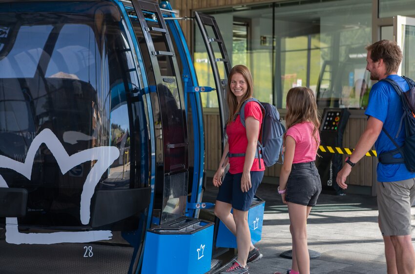 Eine Familie mit Rucksäcken steigt im Sommer in eine blaue Gondel der Natrunbahn am Hochkönig ein, Logo sichtbar auf der Kabine | © Hochkönig Tourismus GmbH