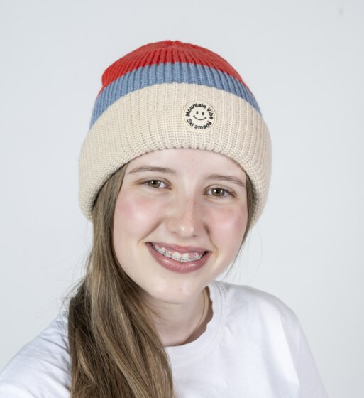 Lächelndes Mädchen mit rot-beiger Mountain Vibe Ski amadé Mütze und weißem Shirt | © Ski amadé GmbH / Lorenz Masser