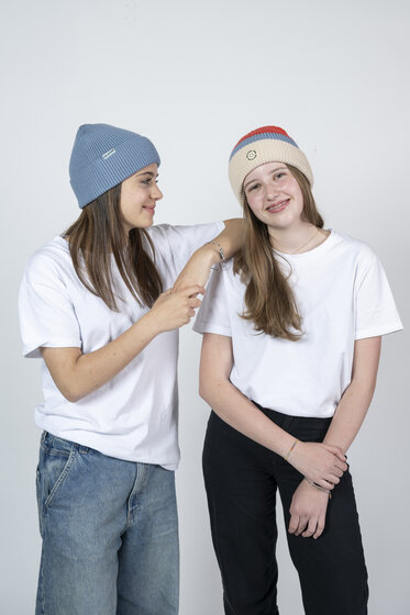 Zwei Mädchen in weißen Shirts mit Ski amadé Mützen stehen lachend nebeneinander | © Ski amadé GmbH / Lorenz Masser