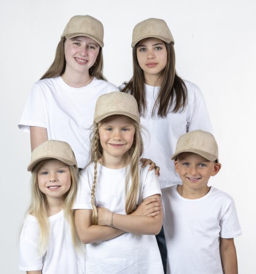 Fünf Kinder tragen beige Baseballcaps und weiße T-Shirts und stehen gemeinsam vor hellem Studiohintergrund | © Ski amadé GmbH / Lorenz Masser