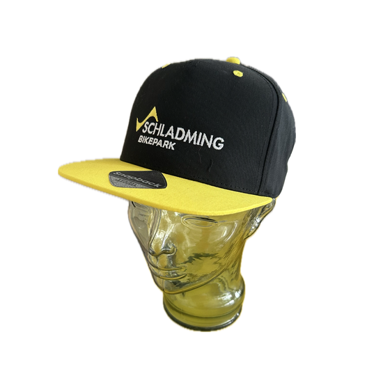 Schwarze Snapback-Kappe mit gelbem Schirm und Bikepark-Stickerei auf Glasmodellkopf präsentiert | © Planai-Hochwurzen-Bahnen GmbH