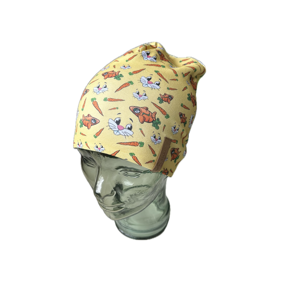 Gelbe Kindermütze auf Glasmodellkopf, bedruckt mit Hasengesichtern, Karotten und orangen Hasenfiguren, Lederlabel seitlich | © Planai-Hochwurzen-Bahnen GmbH