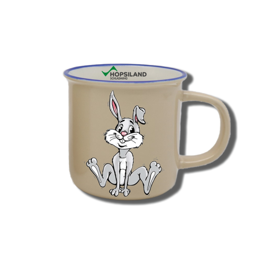 Beigefarbene Kindertasse mit sitzendem Hopsi-Hasen, blauem Rand und Hopsiland-Schriftzug auf der Innenseite | © Planai-Hochwurzen-Bahnen GmbH
