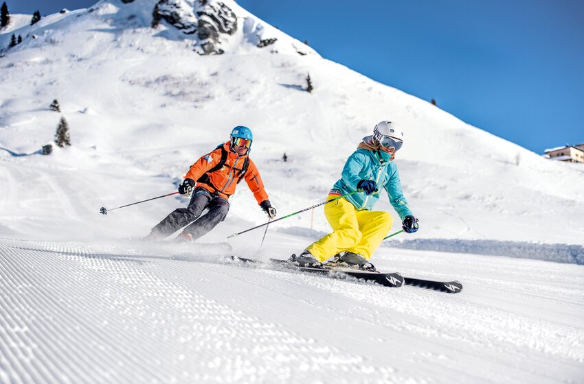 Zwei Skifahrer carven bei Sonnenschein über breite, frisch präparierte Piste mit Pulverschnee. | © Gasteiner Bergbahnen AG