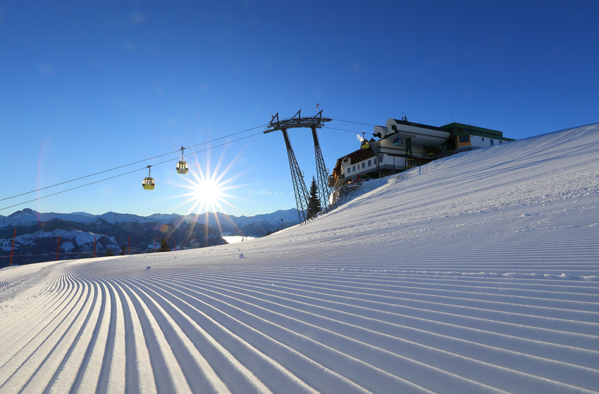 Gondelbahn fährt bei Sonnenaufgang über frisch präparierte Piste zur Bergstation im verschneiten Skigebiet. | © Tourismusverband Großarltal