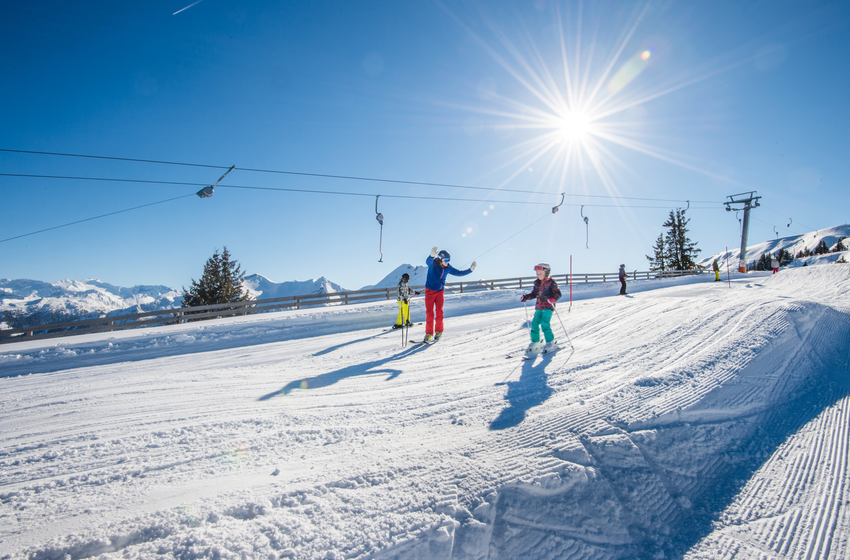 Kinder und Erwachsene fahren bei Sonnenschein auf breiter Skipiste mit Schlepplift im Hintergrund. | © Tourismusverband Großarltal