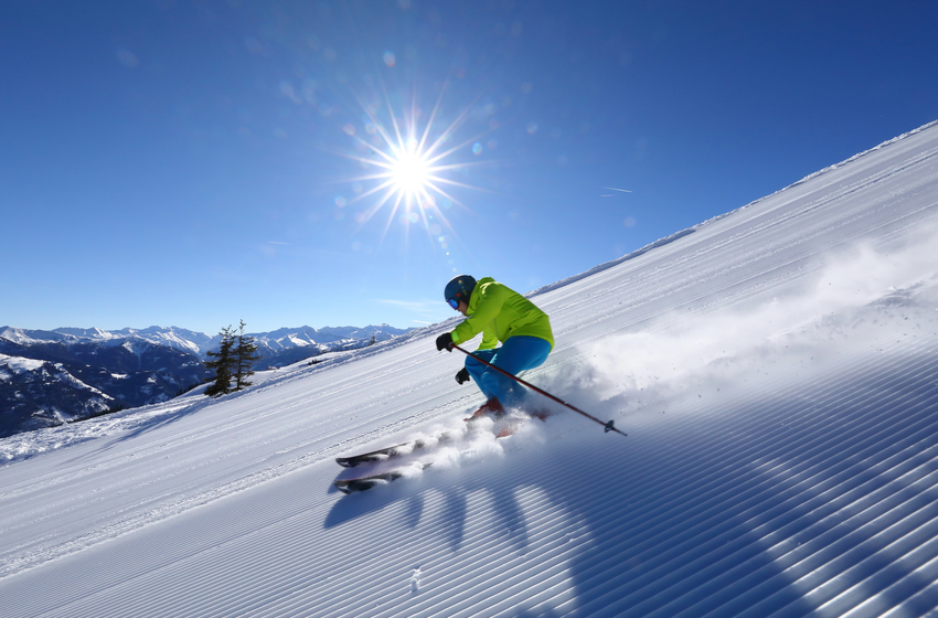 Skifahrer in grüner Jacke carvt durch Pulverschnee auf frisch präparierter Piste bei strahlender Sonne. | © Tourismusverband Großarltal