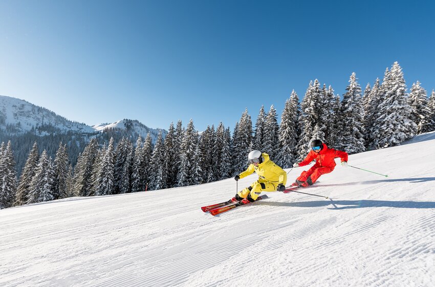 Zwei Skifahrer carven parallel in bunten Anzügen durch frisch präparierten Schnee am Hochkönig. | © Hochkönig Bergbahnen GmbH