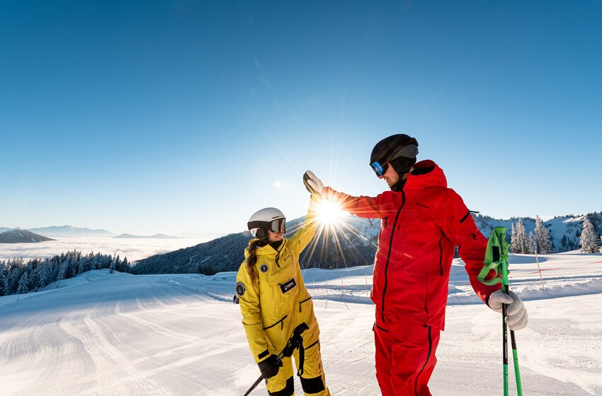 Zwei Skifahrer geben sich ein High-Five bei Sonnenaufgang auf einer perfekt präparierten Piste im Hochkönig. | © Hochkönig Bergbahnen GmbH