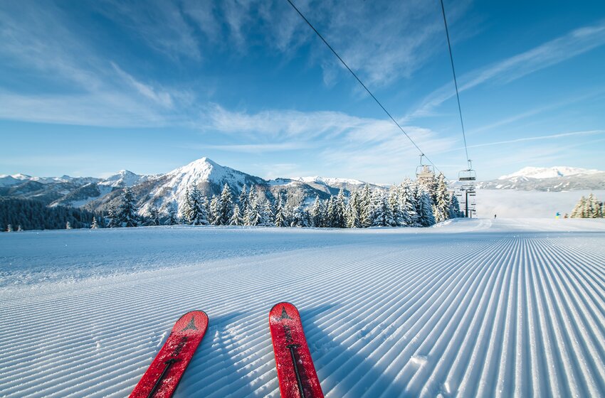 Rote Skier auf frisch präparierter Piste mit Blick auf verschneite Berge und blauen Himmel. | © Salzburger Sportwelt Amadé GmbH