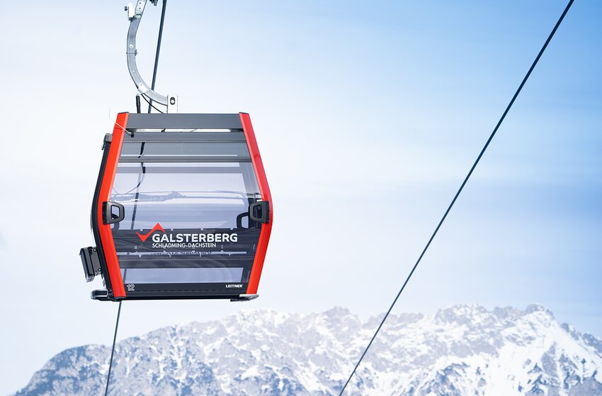Rote Galsterberg-Gondel schwebt vor verschneiter Bergkulisse durch den blauen Himmel in der Region Schladming-Dachstein. | © Galsterbergalm Bahnen GmbH & Co KG 