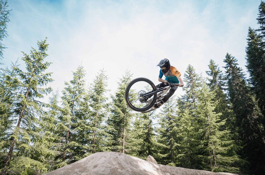 Mountainbiker mit Helm springt auf Reiteralm über Erdhügel, im Hintergrund dichte grüne Nadelbäume. | © Reiteralm Bergbahnen GmbH & Co.KG
