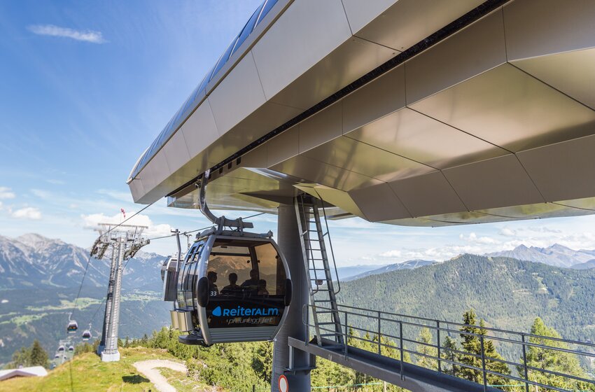 Gondel des Preunegg-Jet auf der Reiteralm schwebt aus moderner Bergstation über grüne Berghänge mit Alpenpanorama. | © Reiteralm Bergbahnen GmbH & Co.KG