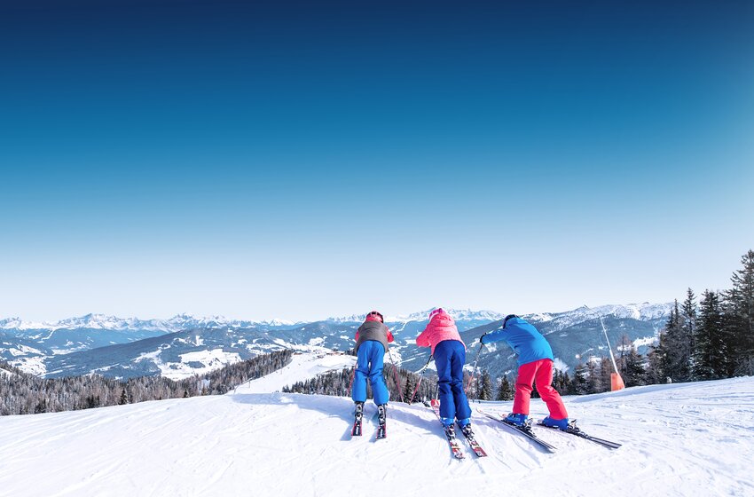 Drei Kinder am Startpunkt einer Skipiste, bereit zur Abfahrt mit Blick über verschneite Berge in Ski amadé. | © Ski amadé GmbH