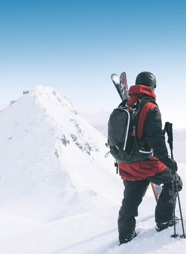 A skier and a snowboarder with helmets and backpacks stand in deep snow, looking at an untouched mountain slope in Ski amadé. | © Ski amadé GmbH