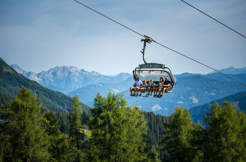 Sechs Personen fahren im Sommer mit der 6er-Gamskogelbahn über grüne Wälder bergauf, mit weitem Blick auf die Bergkulisse. | © Zauchensee Liftgesellschaft Benedikt Scheffer GmbH
