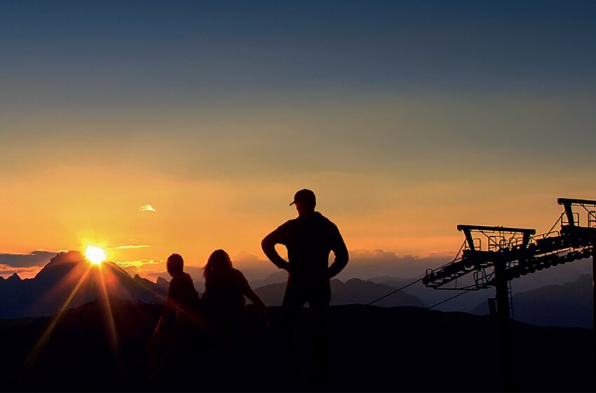Drei Personen und Seilbahn-Silhouette vor farbenprächtigem Sonnenaufgang in alpiner Berglandschaft | © Zauchensee Liftgesellschaft Benedikt Scheffer GmbH