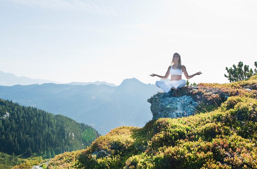 Frau meditiert in weißer Kleidung im Lotussitz auf sonnigem Felsen mit Bergpanorama im Hintergrund | © Zauchensee Liftgesellschaft Benedikt Scheffer GmbH